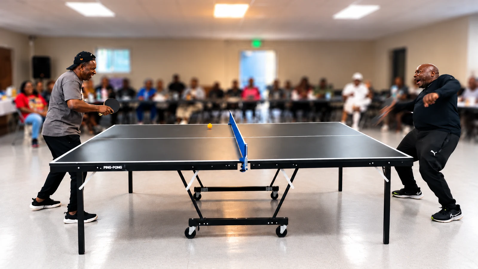Two players rallying at a table tennis table with spectators watching in the softly blurred background